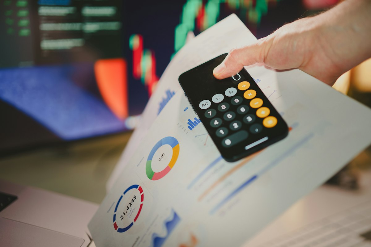 Mano con celular sobre gráficas financieras